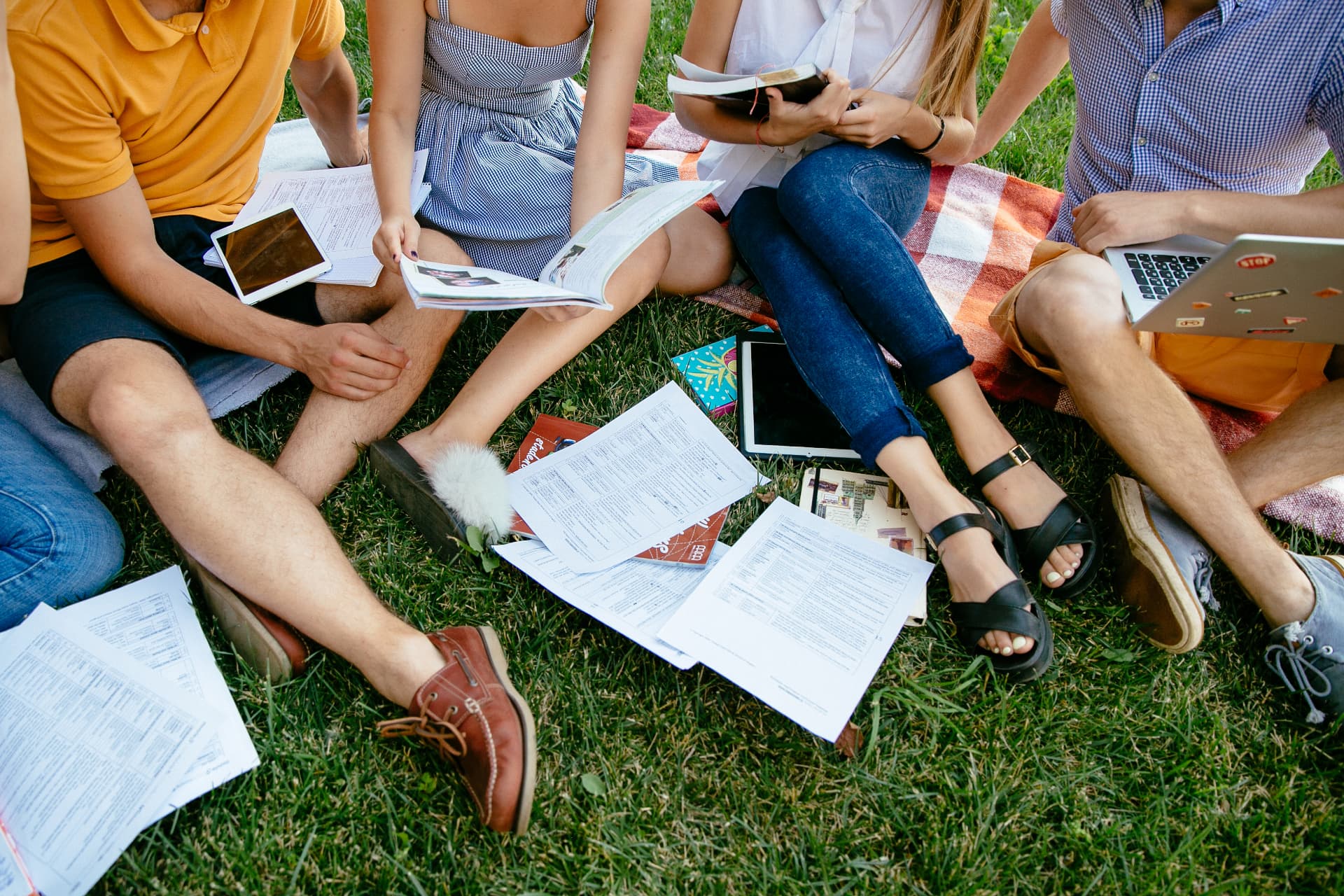 Skupina studentů americké high school učící se společně s poznámkami a tabletem na trávě